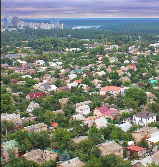 Suburban looking houses intermixed with trees in the foreground, a city in the background.